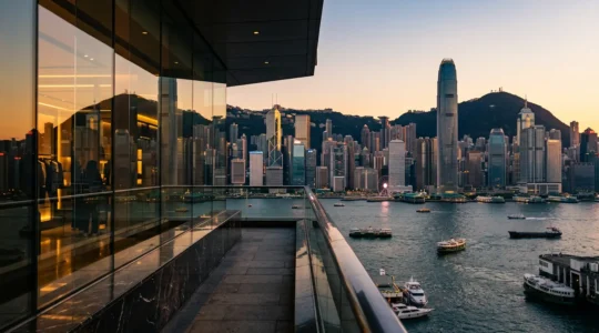 Panoramic view of Hong Kong's harbor skyline with luxury shopping districts reflecting golden light