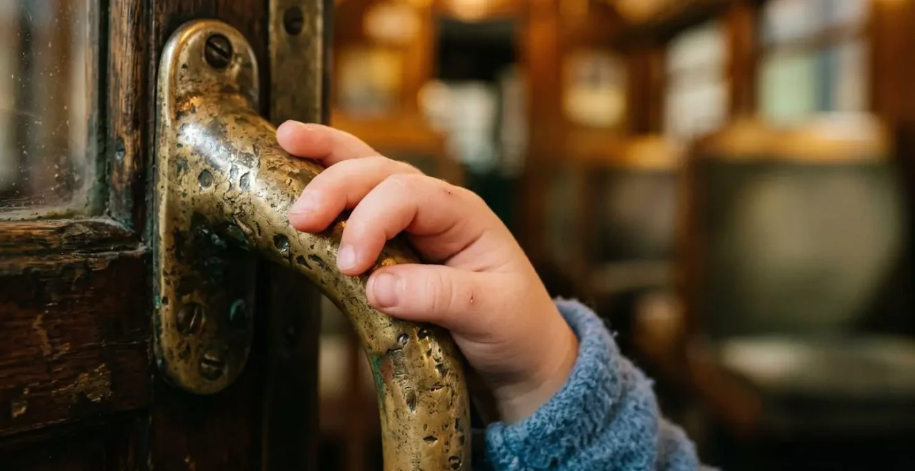 A young child's hand touching the weathered brass handle of a vintage tram display in a museum setting