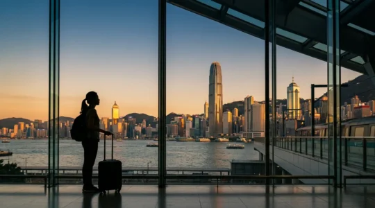 Traveler with luggage viewing Hong Kong skyline at golden hour from airport express platform