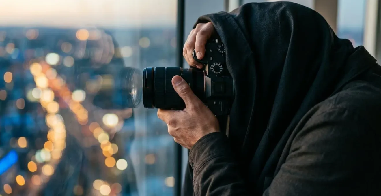 Professional camera setup against glass window capturing night skyline